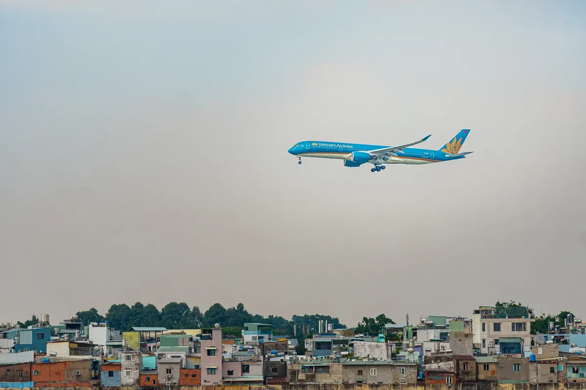 Vietnam Airlines plane flies above cityscape, showcasing air travel over urban housing.