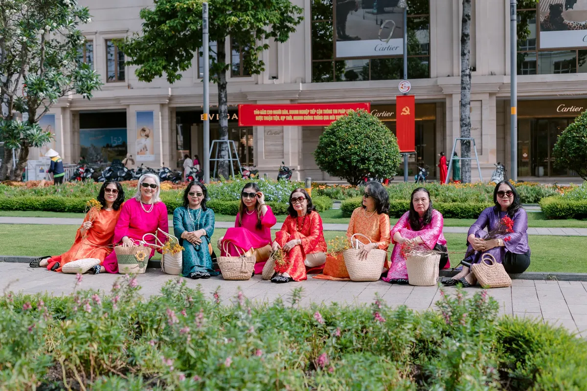 A group of women in colorful Vietnamese dresses sitting outside a city shopping area, enjoying the day.