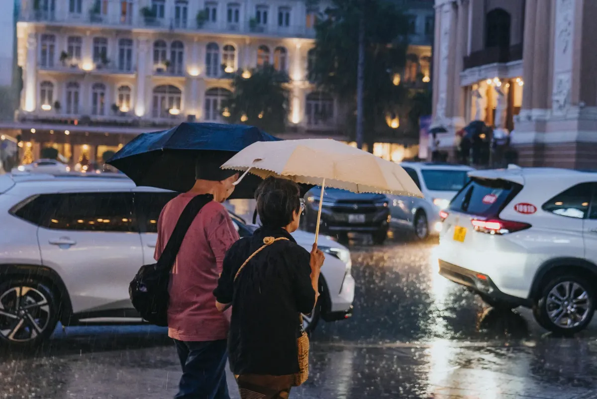 Couple with umbrellas crossing a street on a rainy night in Ho Chi Minh City, Vietnam.
