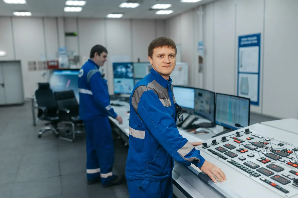 Two technicians operating machinery in a modern control room. Industrial setting with advanced equipment.