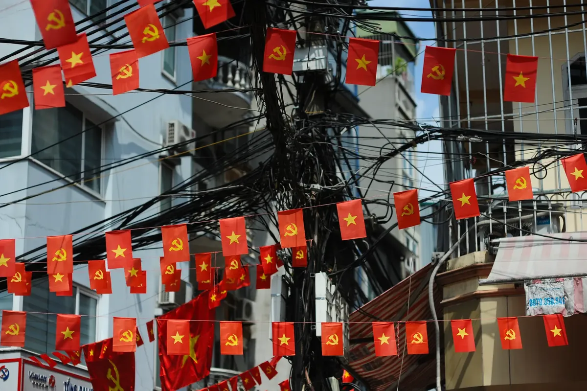 Vibrant red communist flags with yellow stars lining city street amidst tangled power lines.